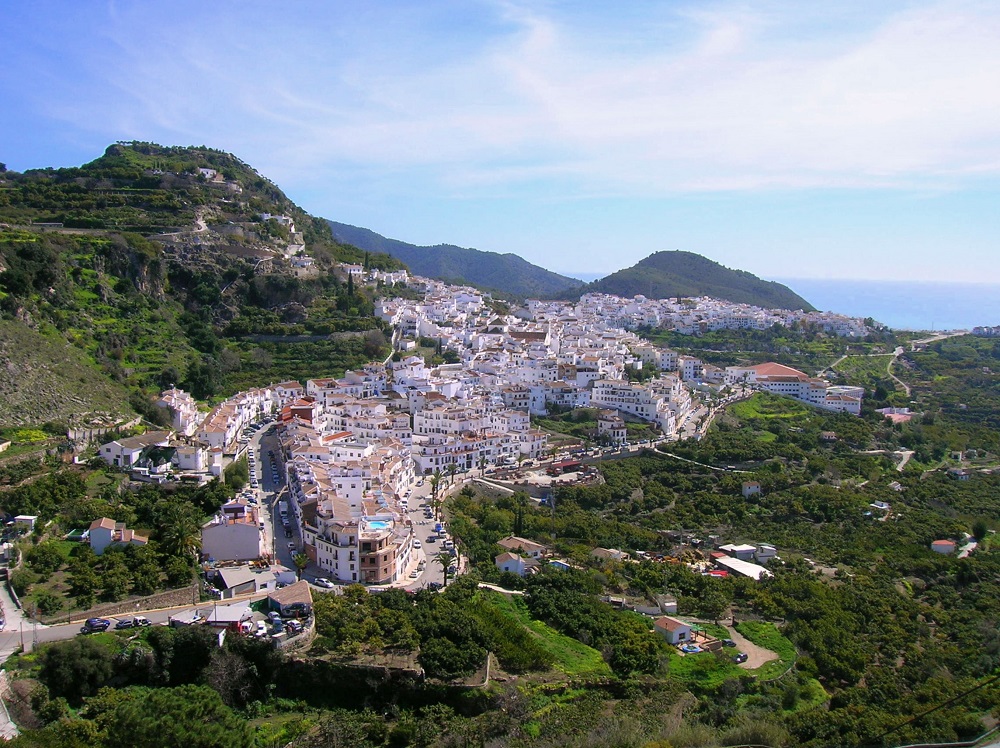 Aerial view of Frigiliana showcasing its white-washed buildings amidst rolling green hills.