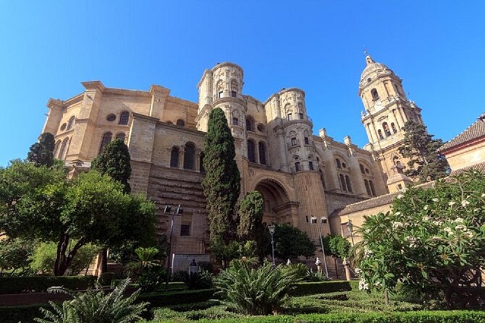 A stunning view of La Manquita, the cathedral of Malaga, with its unique architecture and towering presence against a clear blue sky. The cathedral is surrounded by the vibrant cityscape, showcasing the blend of history and modernity in Malaga.