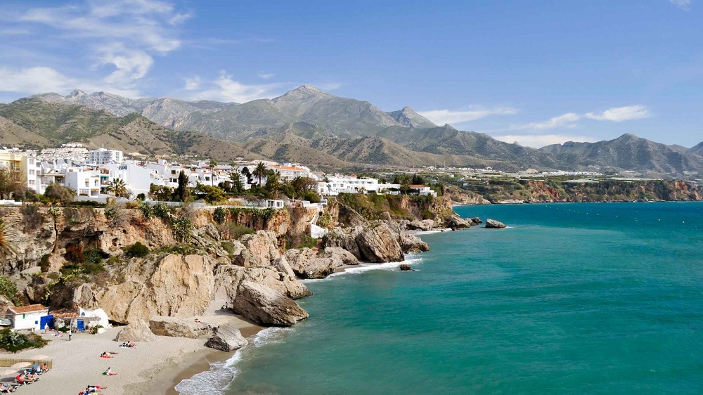 Panoramic view of Nerja's coastline with its pristine beaches, whitewashed buildings, and rugged cliffs against a clear blue sky.