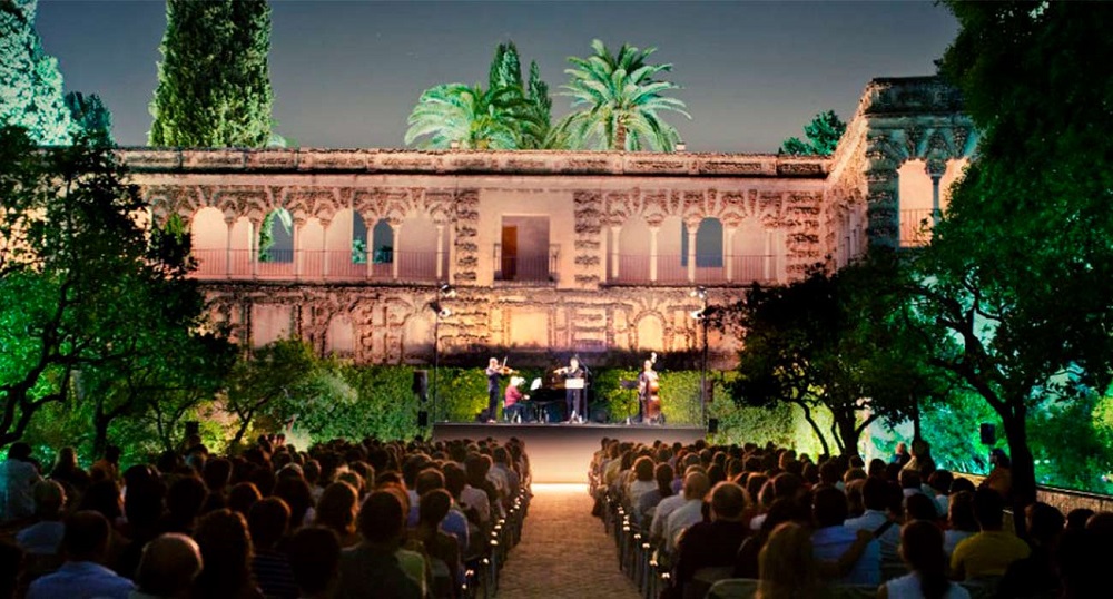 Enchanting evening scene in the gardens of the Real Alcázar, with musicians playing classical tunes under a starlit sky, surrounded by lush greenery and ancient walls.