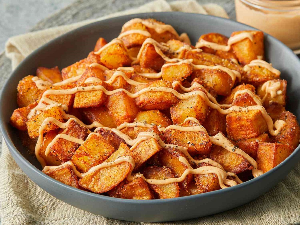 lose-up image of Patatas Bravas, a signature dish in Spanish Cuisine, featuring Spicy Potatoes topped with a rich, red bravas sauce, served on a rustic ceramic plate.