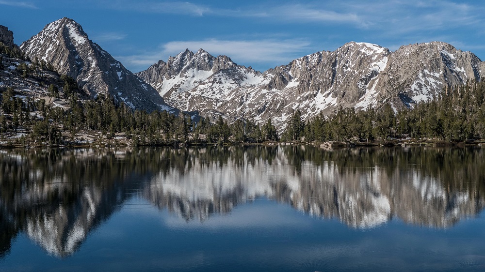A breathtaking view of the Sierra Nevada mountain range, with snow-capped peaks against a clear blue sky, and a lush green forest and beautiful lake in the foreground.