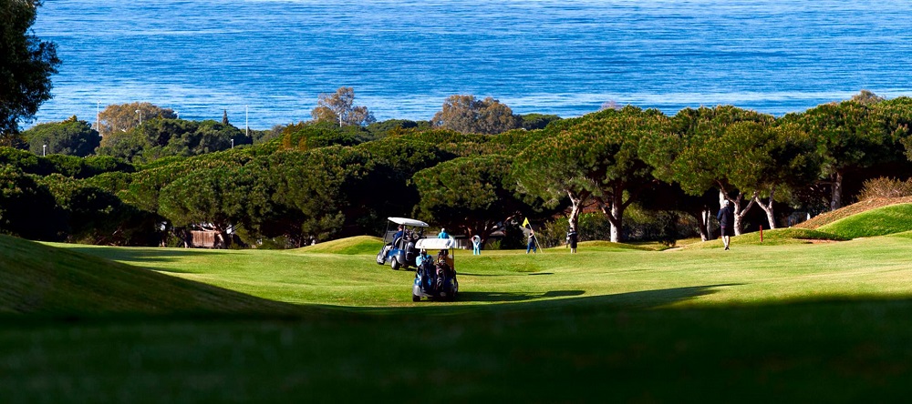 Golfers teeing off at Cabopino Golf Marbella with the shimmering Mediterranean Sea in the background.
