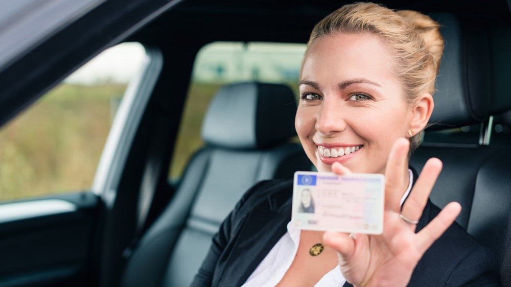 A radiant woman proudly displaying her newly acquired Spanish driver's license inside a car.