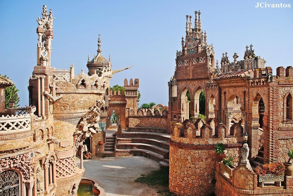 Panoramic view of Castillo de Colomares against a clear blue sky, showcasing its intricate architectural details and lush surrounding gardens.